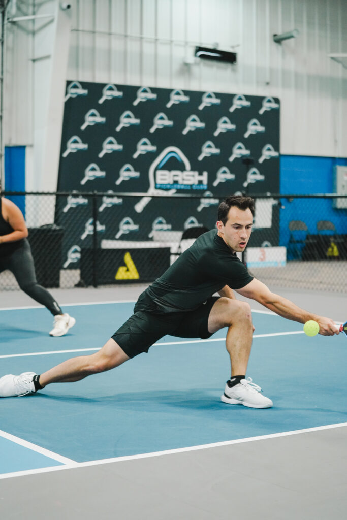 League Premier Division player stretches to return a low shot during a Match Point League match at Bash Pickleball Club in Michigan.